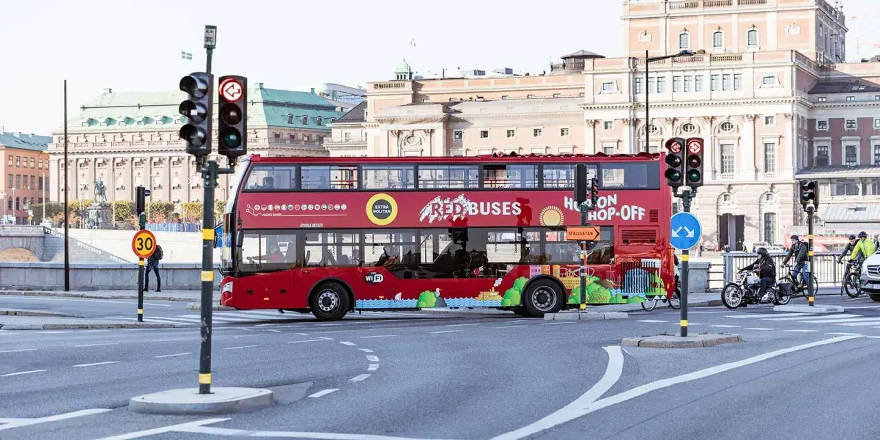 Röd dubbeldäckare med texten "Hop On Hop Off" kör genom staden.