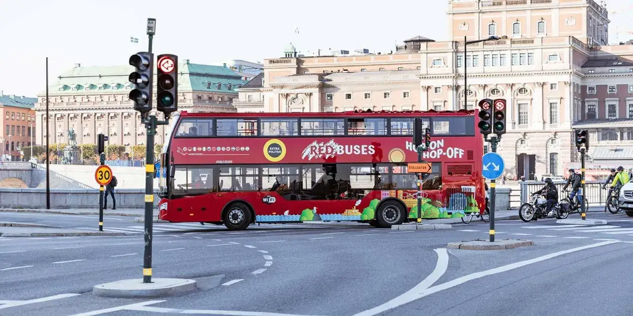 Röd dubbeldäckare med texten "Hop On Hop Off" kör genom staden.