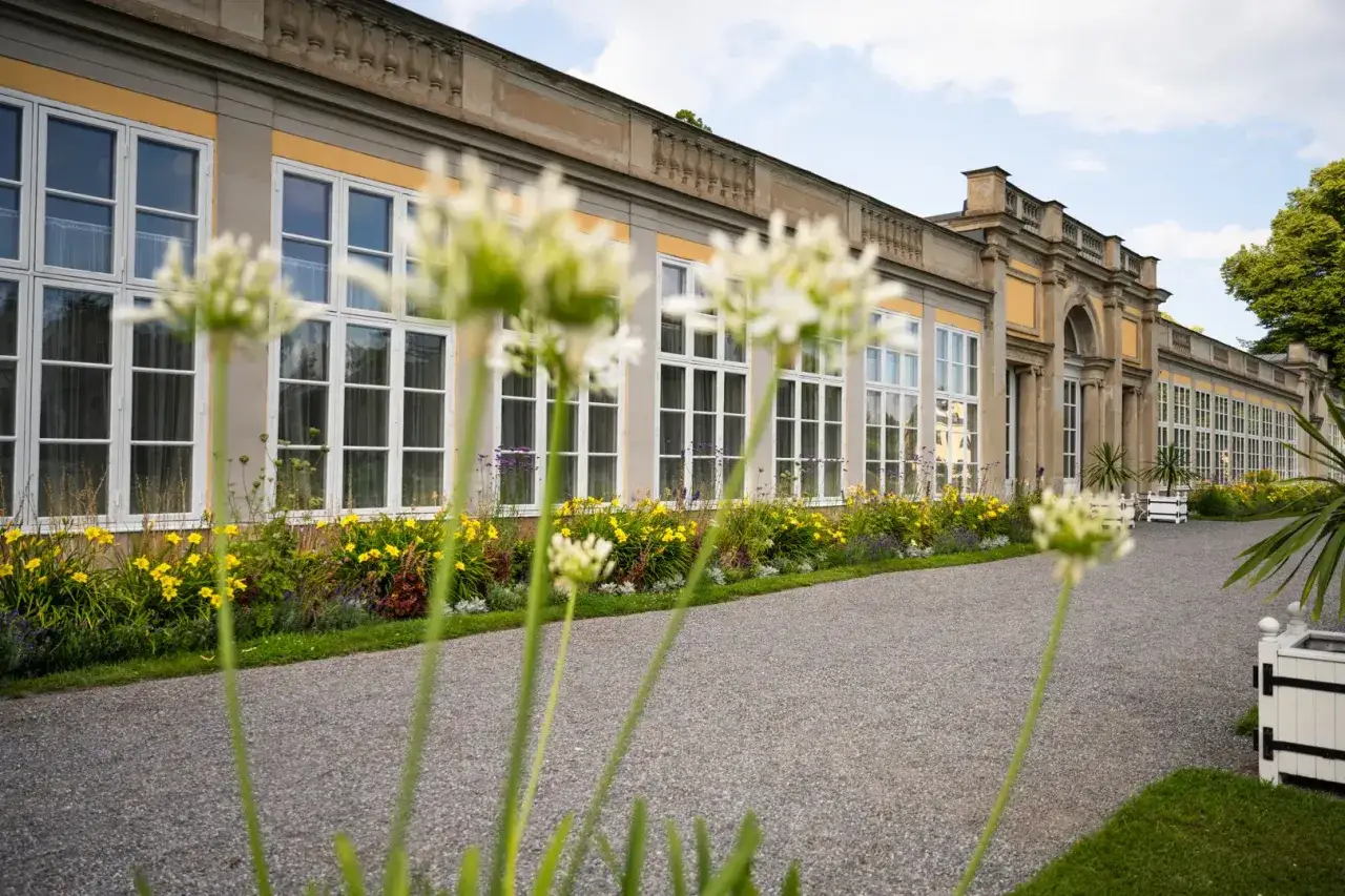 Vacker fasad med stora fönster på Ulriksdals slott, kantad av blommor och grönska.