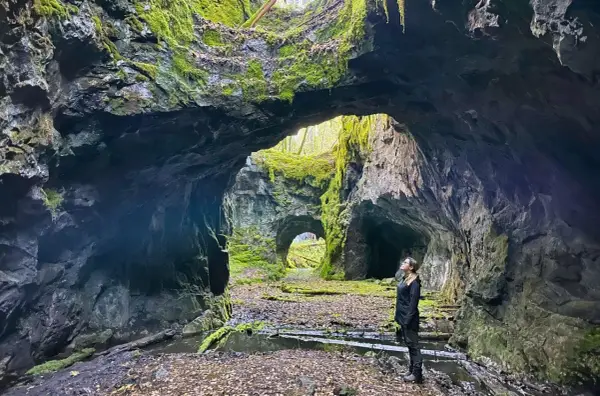 En kvinna står i en mossig grotta, en del av **Tilas stoll**, och blickar upp mot ljuset som sipprar in.